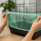 Close-up of hands fitting a green mesh bird cage seed catcher around the lower section of a bird cage.