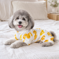 Grey small dog relaxing on a bed while wearing yellow duck-print cotton pyjamas